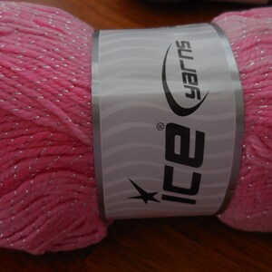 Puede incluir: Un hilo rosa con hilo plateado, etiquetado "ICE Yarns" en una etiqueta blanca con una estrella.