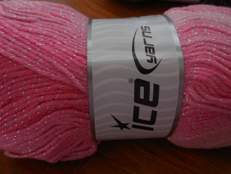Puede incluir: Un hilo rosa con hilo plateado, etiquetado "ICE Yarns" en una etiqueta blanca con una estrella.