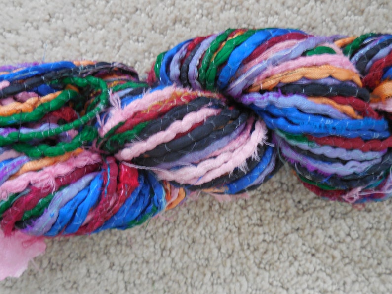 May include: A skein of colorful yarn made from recycled fabric scraps. The yarn is a mix of blue, green, pink, purple, red, and orange.