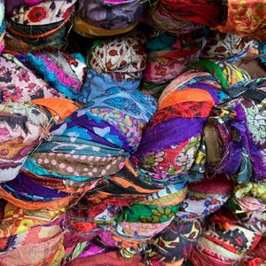May include: Close-up of a collection of colorful fabric scraps, tightly bundled and woven together. The textiles display a variety of patterns and colors, including pink, purple, orange, and blue. The image showcases a handmade craft or textile art piece.