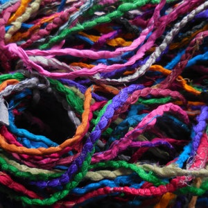 May include: A close-up of a bundle of colorful fabric yarn. The yarn is made of various colors, including pink, blue, green, orange, and purple. The yarn is twisted and knotted together, creating a textured and intricate pattern.