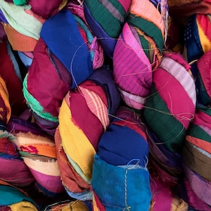 May include: Close-up of colorful fabric bundles. The bundles are made of various fabrics in shades of blue, pink, green, yellow, and red. The fabric appears to be wrapped and tied, creating a textured and layered effect. The image is well-lit, highlighting the vibrant colors.