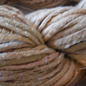 May include: A close-up of a bundle of beige silk ribbon yarn with gold metallic thread woven throughout.