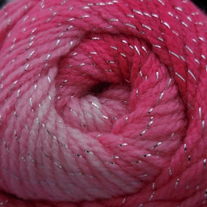 Puede incluir: Un ovillo de hilo rosa y blanco con hilo plateado que lo atraviesa.