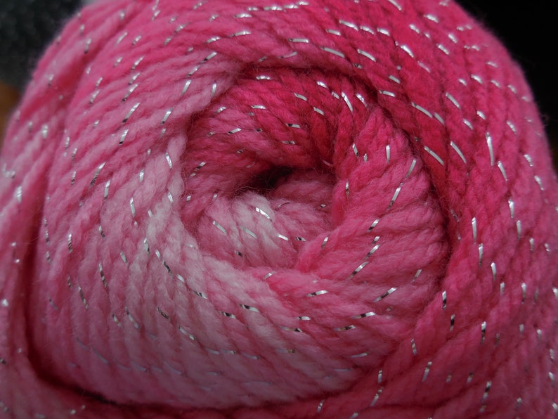 Puede incluir: Un ovillo de hilo rosa y blanco con hilo plateado que lo atraviesa.