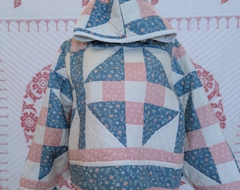 May include: A hooded pullover jacket constructed from quilted fabric featuring a patchwork design. The pattern consists of alternating squares and triangles in dusty blue with small floral prints, soft pink with tiny white dots, and solid cream.