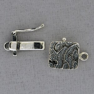 May include: Silver tone clasp with a textured square design and a hook closure. The clasp is designed for jewelry making.