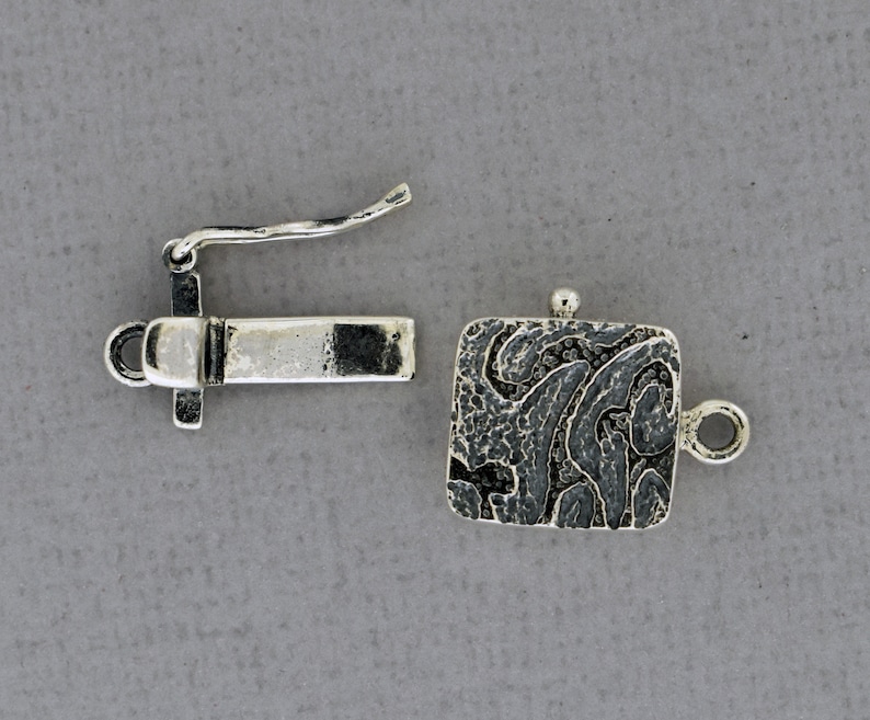 May include: Silver tone clasp with a textured square design and a hook closure. The clasp is designed for jewelry making.