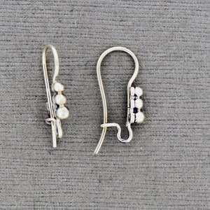 Peut inclure: Une paire de crochets d'oreille en argent avec trois petites perles rondes sur chaque crochet.