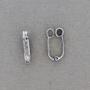 May include: Silver-toned metal clasp with a decorative design. The clasp has two loops on one end and a single loop on the other end.