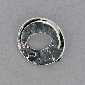 May include: A silver ring with a textured, hammered finish. The ring is shaped like a circle with a gap in the middle, creating a unique and modern design.