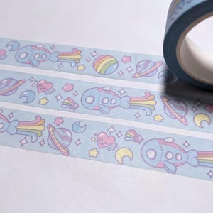 May include: A roll of blue washi tape with a repeating pattern of pastel-colored planets, stars, hearts, rainbows, and cartoon spaceships.