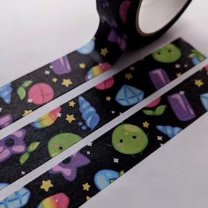 Peut inclure: Ruban washi avec un fond noir et un motif répété de pierres précieuses colorées, d'étoiles et de mignonnes créatures vertes.