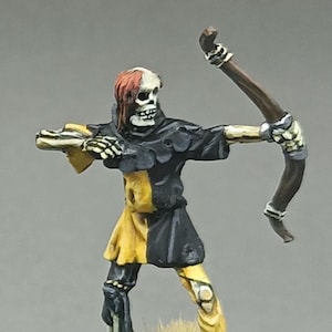 Pode incluir: Miniatura de um arqueiro esqueleto em traje preto e amarelo, segurando um arco. A figura tem uma cabeça de caveira com cabelo ruivo e está montada em uma base texturizada com grama. Colecionável de fantasia.