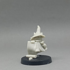 Könnte beinhalten: Eine kleine, unbemalte Figur eines Zauberers, der eine Schriftrolle hält. Der Zauberer trägt einen spitzen Hut und einen Umhang. Die Figur ist auf einem schwarzen, kreisförmigen Sockel montiert.