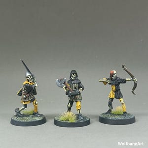 Pode incluir: Três figuras de esqueletos em miniatura, cada uma posando com uma arma. Uma segura uma lança, outra um machado e a terceira um arco e flechas. Usam armaduras pretas e amarelas e estão em bases redondas com relva.