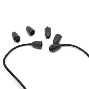 May include: A collection of black cord end caps and cord locks. The caps are cone-shaped with a rounded tip, and the locks have a cylindrical base. The caps and locks are made of a smooth, matte material. A black cord is attached to one of the cord locks.