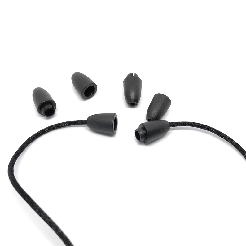 May include: A collection of black cord end caps and cord locks. The caps are cone-shaped with a rounded tip, and the locks have a cylindrical base. The caps and locks are made of a smooth, matte material. A black cord is attached to one of the cord locks.