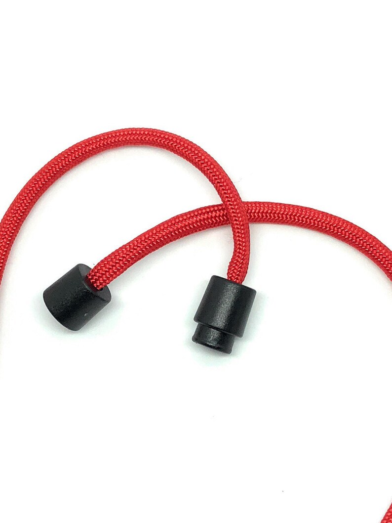 May include: Close-up of a red cord with two black plastic end pieces. The cord is thick and braided, and the end pieces are cylindrical. The background is plain white.