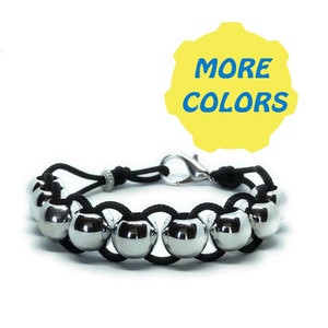 May include: A bracelet featuring large, shiny silver metal beads strung on a black cord. The bracelet has a silver clasp and a small, decorative silver bead. The image includes a yellow shape with the words "MORE COLORS" in blue.