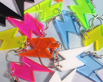 May include: A collection of colorful lightning bolt earrings in various shades, including black, orange, pink, green, blue, and white. Each earring features a silver-tone hook. The earrings are made of a translucent material.