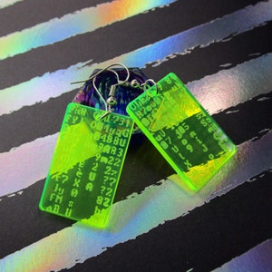 May include: A pair of neon green acrylic earrings with silver hooks. The earrings are rectangular and feature a random assortment of letters and numbers.