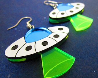 May include: A pair of silver earrings shaped like flying saucers with a blue and white design and a neon green bottom.