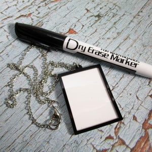 May include: A silver chain necklace with a black frame and white dry erase board pendant. The pendant is attached to the chain with a silver clasp. A black dry erase marker is included. "For Whiteboards Dry Erase Marker" is printed on the marker.