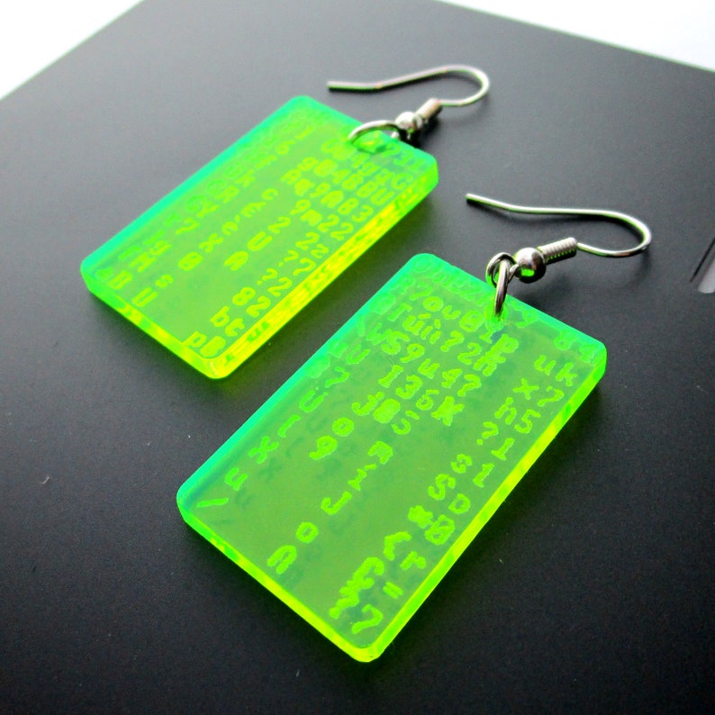 May include: A pair of neon green acrylic earrings with a rectangular shape. The earrings have a silver hook and feature a pattern of numbers and letters.