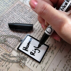 May include: A white dry-erase tag with a black chain attached. The tag has the words "Human Rights" written on it in black marker.