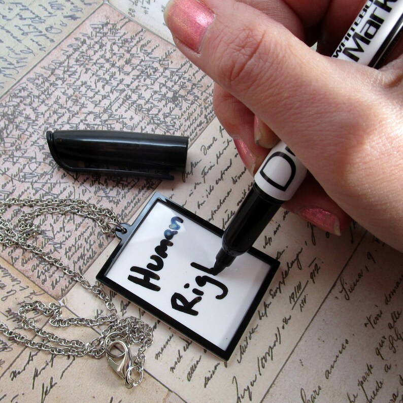 May include: A white dry-erase tag with a black chain attached. The tag has the words "Human Rights" written on it in black marker.
