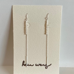 May include: A pair of silver chain earrings with a small bar at the bottom. The earrings are displayed on a white card with the text "helen wang" written in black.