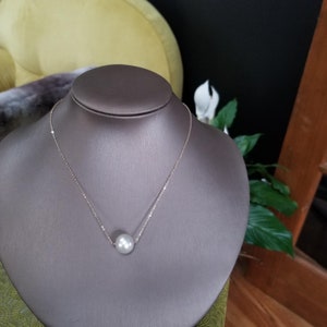 May include: A delicate gold chain necklace with a single large white pearl pendant.