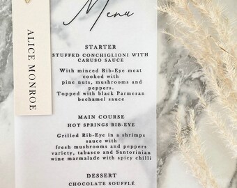 May include: A wedding menu card with a white background and black text. The menu includes a starter, main course, and dessert. The starter is stuffed conchiglioni with caruso sauce. The main course is hot springs rib-eye. The dessert is chocolate souffle.