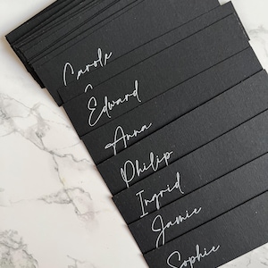 Marque-places noirs avec étiquettes de nom de menu à l'encre blanche