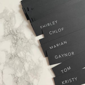Marque-places noirs avec étiquettes de nom de menu à l'encre blanche