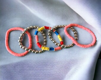 May include: Five colorful bracelets with silver beads. The bracelets are pink, yellow, blue, and red. They are stacked on top of each other.