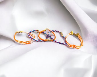 Può includere: Quattro braccialetti intrecciati con dettagli dorati. I braccialetti sono arancioni, bianchi e blu.