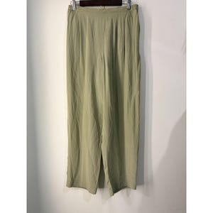 May include: Sage green trousers featuring a high-waisted design with an elastic waistband and subtle vertical pleats extending from the waist. These full-length pants have a relaxed, straight-leg silhouette and are suspended from a dark hanger.