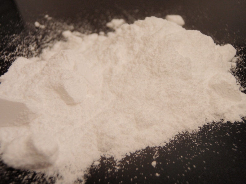 Puede incluir: Primer plano de un polvo blanco, probablemente bicarbonato de sodio o maicena, sobre una superficie negra.