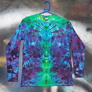 May include: A long-sleeved shirt with a tie-dye pattern in shades of purple, blue, and green. The shirt has a symmetrical design with a green centre and a dark purple outer edge.