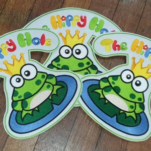 May include: Three white felt patches with a green frog wearing a gold crown and sitting on a blue lily pad. Each patch has the text "The Hippy Hole" in colorful letters.