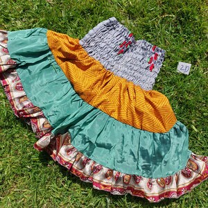 May include: A multi-layered skirt with a grey elastic waistband, featuring a green, yellow and red paisley print. The skirt has a ruffled hem and is made of a soft, flowing fabric.