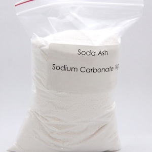 Puede incluir: Una bolsa de pl&aacute;stico blanca llena de polvo blanco con la etiqueta "Soda Ash Sodium Carbonate 1kg".