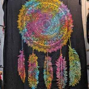 May include: Black tapestry featuring a vibrant, rainbow-colored mandala design. The mandala is surrounded by a yellow and orange border, with pink, blue, and green accents. Below the mandala are five colorful feathers.