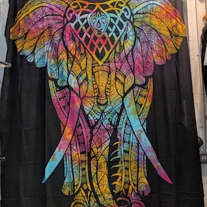 May include: A black tapestry featuring a vibrant, colorful elephant design. The elephant is depicted with intricate patterns in shades of pink, yellow, blue, and orange. The tapestry is hanging on a wooden rod.