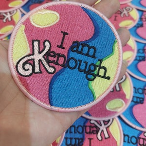 Könnte beinhalten: Ein gestickter Aufnäher in Rosa und Blau mit dem Text "I am enough" in schwarzen Buchstaben. Der Aufnäher hat ein Wirbeldesign und einen gelben Akzent.