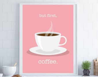 May include: A framed print featuring a white coffee cup on a saucer, filled with dark liquid, against a pink background. The words "but first," and "coffee." are written in white. The print is displayed in a kitchen setting.