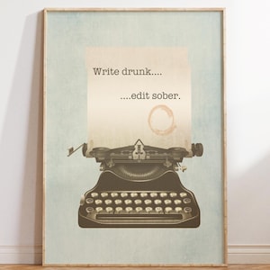 May include: A framed print showing a vintage typewriter with a sheet of paper. The paper has the text "Write drunk....edit sober." printed on it, along with a coffee stain. The background is a light blue and beige.