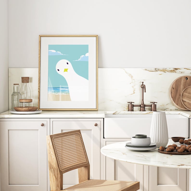 Puede incluir: Una ilustraci&oacute;n enmarcada de una gaviota blanca con un pico amarillo mirando por encima del hombro al espectador. La gaviota est&aacute; de pie en una playa con agua azul y nubes blancas en el fondo.